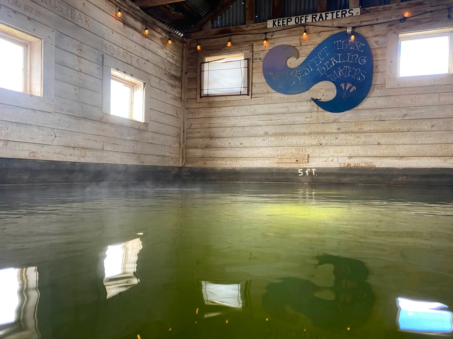 Inside the historic Summer Lake bathhouse — steaming geothermal pool with 'Respect These Healing Waters' sign