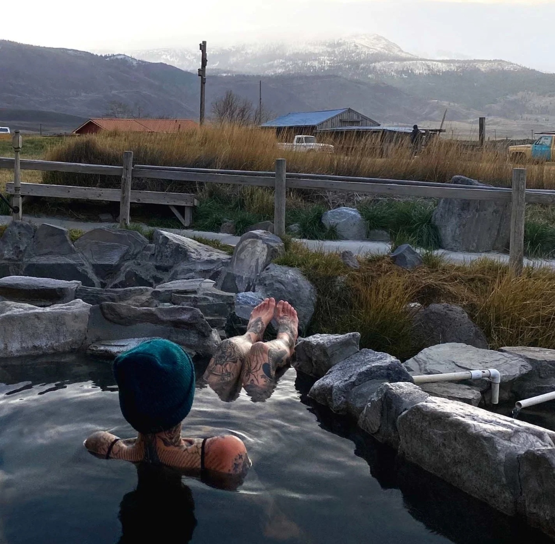 Person soaking in a rock pool at Summer Lake Hot Springs with mountain view