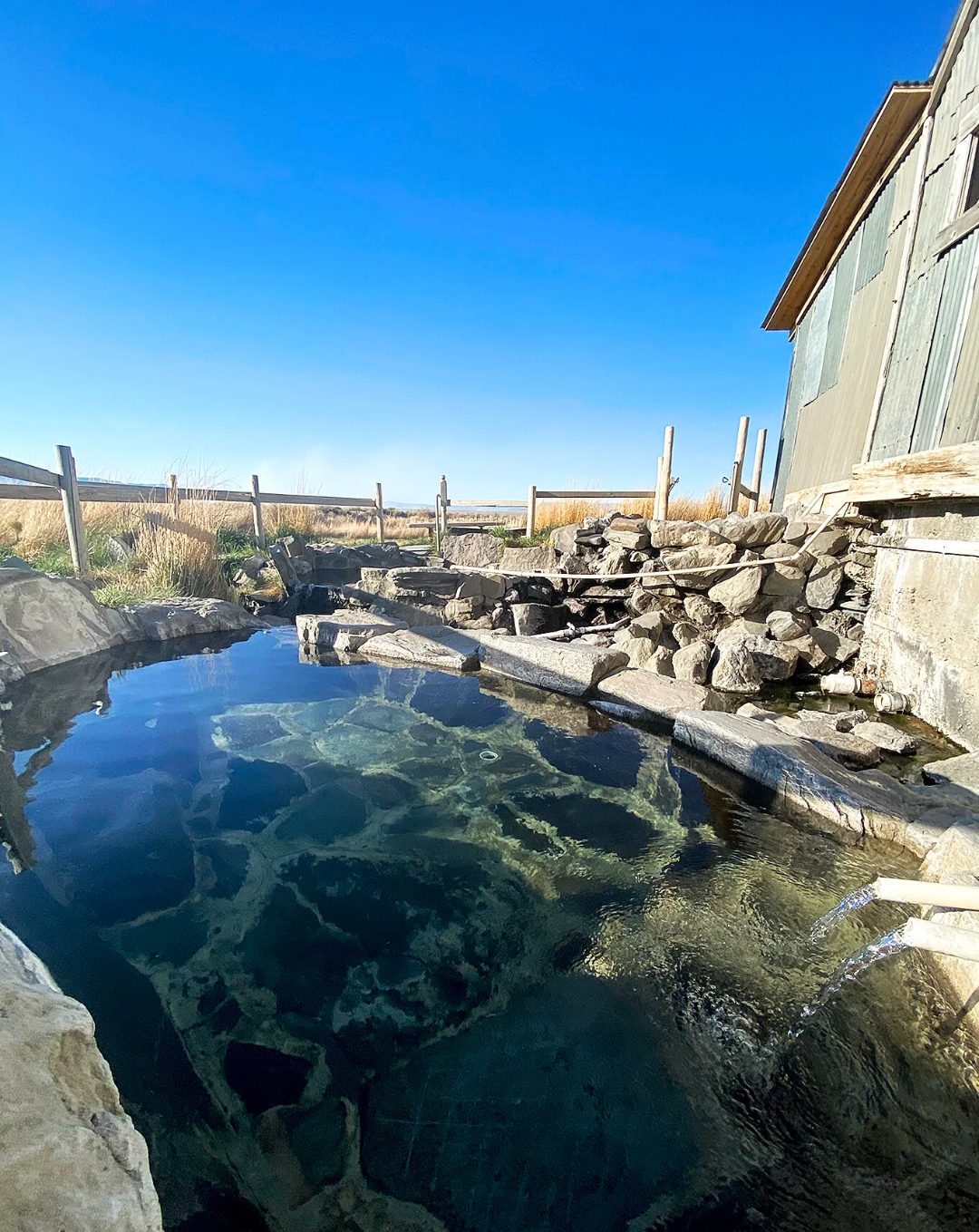Outdoor soaking pool at Summer Lake Hot Springs with blue sky reflection