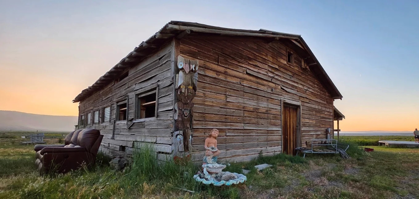 Rustic old barn with totem pole and mermaid statue at Summer Lake at sunset